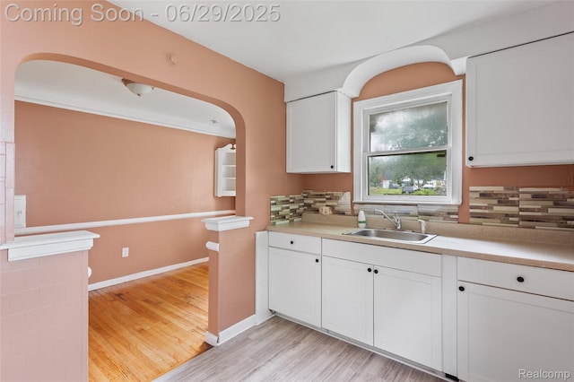 16746 Bramell St, Detroit, MI 48219 - kitchen featuring backsplash, light wood-type flooring, white cabinets, arched walkways, and light countertops