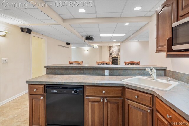17601 Rolling Woods Cir, Northville, MI 48168 - kitchen with black dishwasher, stainless steel microwave, a paneled ceiling, brown cabinetry, and a fireplace
