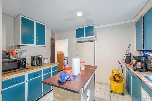 735 W Stewart St, Owosso, MI 48867 - kitchen featuring stainless steel microwave, blue cabinetry, butcher block counters, freestanding refrigerator, and crown molding