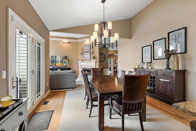 7870 Mooring Ct, Hudsonville, MI 49426 - dining area with light wood finished floors, a chandelier, high vaulted ceiling, and a warm lit fireplace