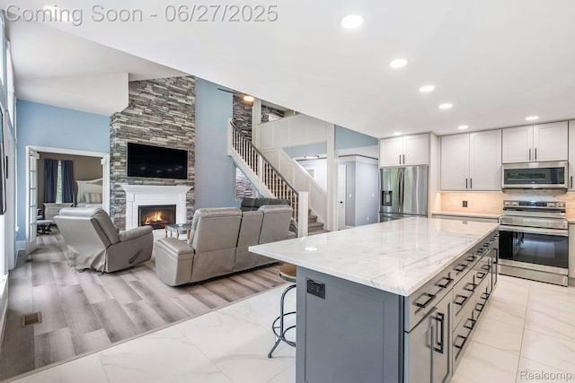 5408 N Seymour Rd, Flushing, MI 48433 - kitchen with appliances with stainless steel finishes, a large fireplace, open floor plan, light stone counters, and decorative backsplash