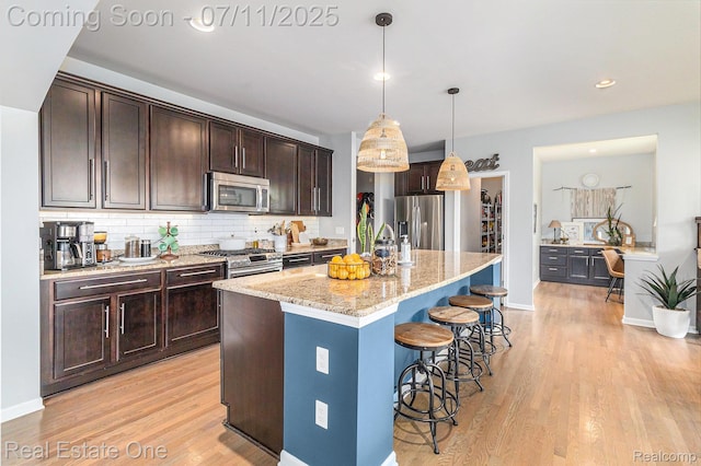 59141 Peters Barn Dr, South Lyon, MI 48178 - kitchen featuring appliances with stainless steel finishes, light wood finished floors, light stone counters, dark brown cabinetry, and a kitchen breakfast bar