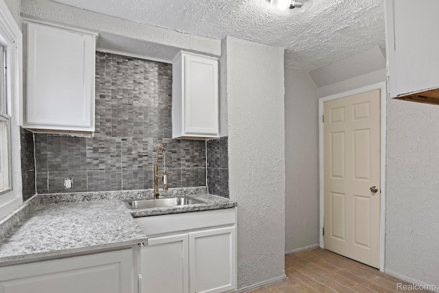 9110 Mansfield St, Detroit, MI 48228 - kitchen with light wood-style floors, decorative backsplash, white cabinets, a textured wall, and a textured ceiling