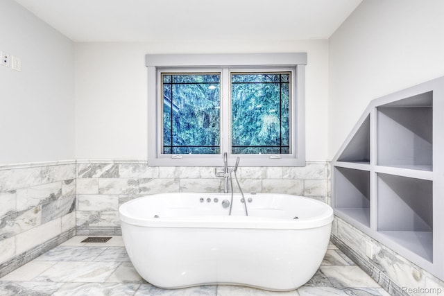2685 Fry Rd, Highland, MI 48357 - bathroom with marble tiled flooring, a freestanding tub, wainscoting, and tile walls