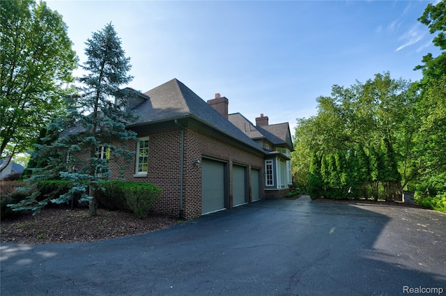 8356 Misty Mdws, Grand Blanc, MI 48439 - view of side of property featuring brick siding, a garage, a chimney, asphalt driveway, and a shingled roof