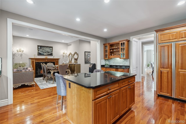 8356 Misty Mdws, Grand Blanc, MI 48439 - kitchen featuring light wood-type flooring, dark countertops, brown cabinets, glass insert cabinets, and a kitchen breakfast bar