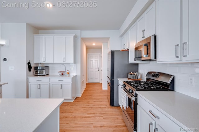 606 Angus Ln, Saline, MI 48176 - kitchen featuring appliances with stainless steel finishes, light wood finished floors, light countertops, white cabinets, and backsplash