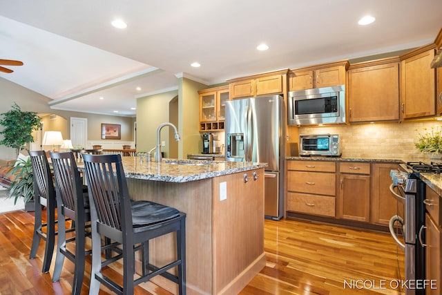 7150 Limerick Ln SW, Byron Center, MI 49315 - kitchen featuring stainless steel appliances, a breakfast bar, light wood finished floors, decorative backsplash, and light stone countertops