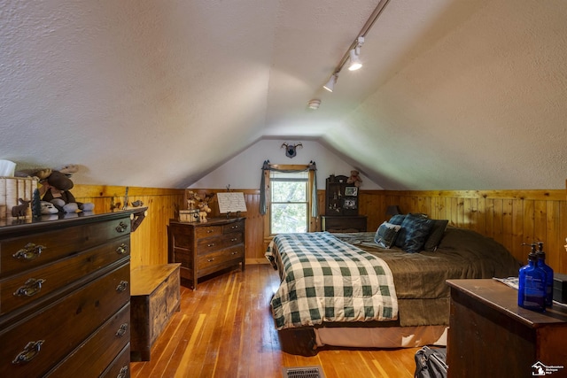 2030 W Sterns Rd, Temperance, MI 48182 - bedroom with wood walls, a textured ceiling, light wood-style flooring, lofted ceiling, and rail lighting