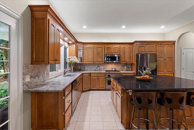 4608 Old Grand River Trl NE, Ada, MI 49301 - kitchen featuring appliances with stainless steel finishes, dark stone countertops, decorative backsplash, brown cabinetry, and recessed lighting