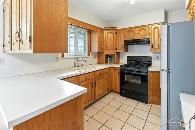 2295 Plainview Dr, Saginaw, MI 48603 - kitchen with black gas range oven, freestanding refrigerator, under cabinet range hood, light tile patterned flooring, and brown cabinetry