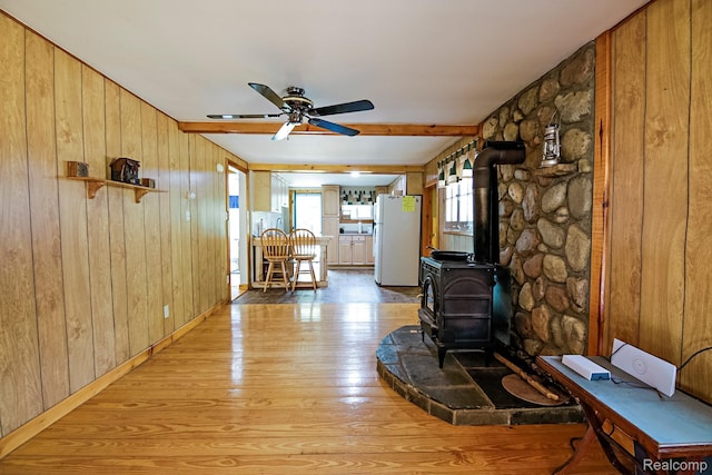 4176 Kings Corner Rd, Glennie, MI 48737 - living area with a wood stove, light wood-type flooring, wooden walls, a ceiling fan, and beam ceiling