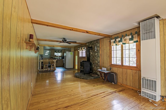4176 Kings Corner Rd, Glennie, MI 48737 - unfurnished living room with a heating unit, wood walls, light wood-style flooring, a wood stove, and beam ceiling