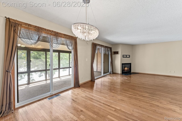 510 Cliffs Dr Unit 305, Ypsilanti, MI 48197 - unfurnished living room featuring a textured ceiling, light wood-style flooring, a chandelier, and a glass covered fireplace