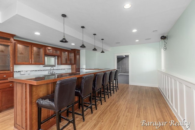 8790 Laurel Ridge Dr SE, Alto, MI 49302 - kitchen with light wood-style flooring, brown cabinets, a breakfast bar area, recessed lighting, and hanging light fixtures