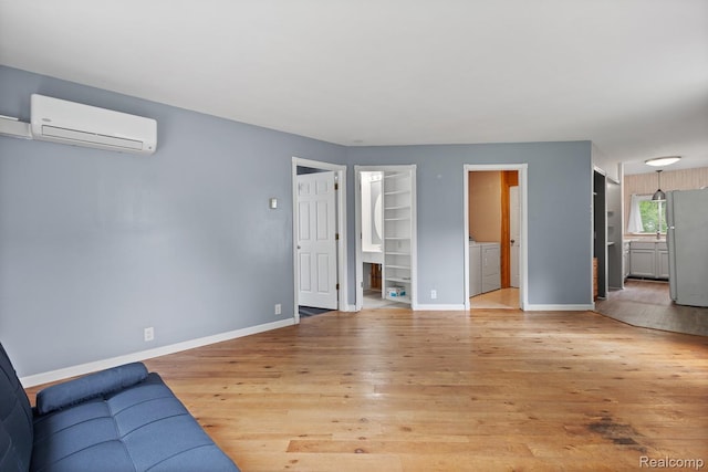 830 College Ave, Adrian, MI 49221 - unfurnished living room featuring an AC wall unit, light wood-type flooring, washing machine and clothes dryer, and built in shelves