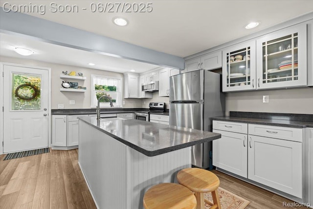 1500 Clark Lake Rd, Brighton, MI 48114 - kitchen featuring appliances with stainless steel finishes, dark countertops, light wood-style flooring, a breakfast bar, and glass insert cabinets