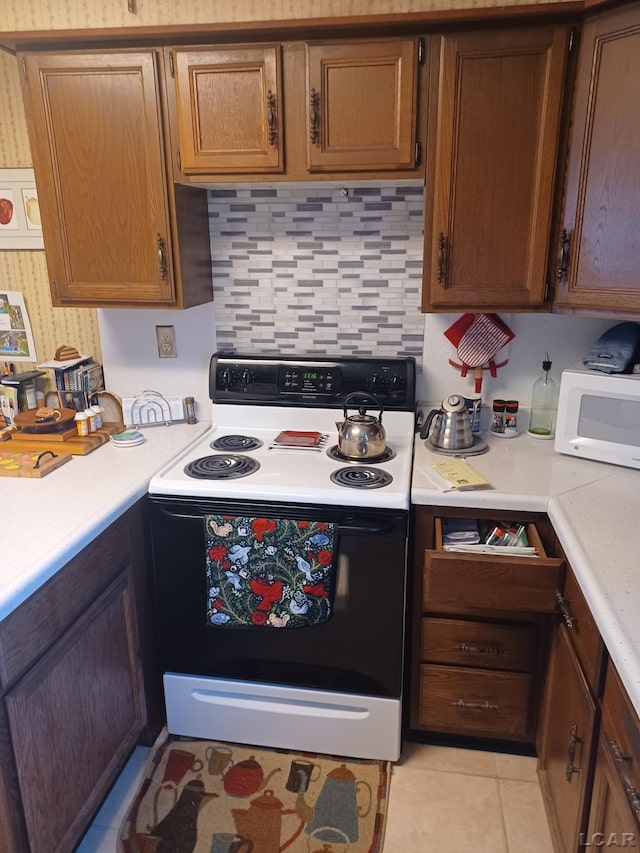 526 Comstock St, Adrian, MI 49221 - kitchen with black range with electric cooktop, white microwave, light countertops, backsplash, and light tile patterned floors