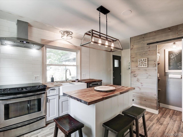 3107 Stone St, Port Huron, MI 48060 - kitchen with butcher block counters, stainless steel range with electric stovetop, wall chimney exhaust hood, light wood-style flooring, and white cabinets