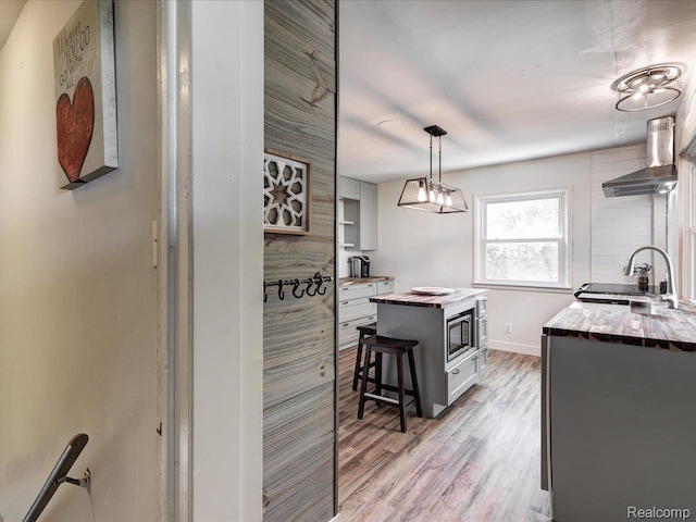 3107 Stone St, Port Huron, MI 48060 - kitchen featuring wall chimney exhaust hood, light wood-style floors, stainless steel microwave, butcher block counters, and open shelves