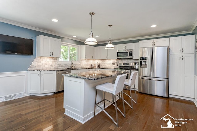 7007 Jackman Rd, Temperance, MI 48182 - kitchen featuring appliances with stainless steel finishes, ornamental molding, dark wood-type flooring, dark stone countertops, and a kitchen bar