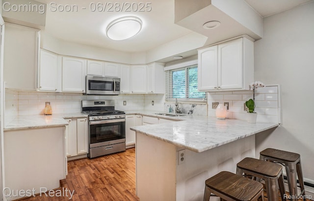 181 S Josephine Ave, Pontiac, MI 48341 - kitchen with stainless steel appliances, a peninsula, a breakfast bar, light wood finished floors, and white cabinets