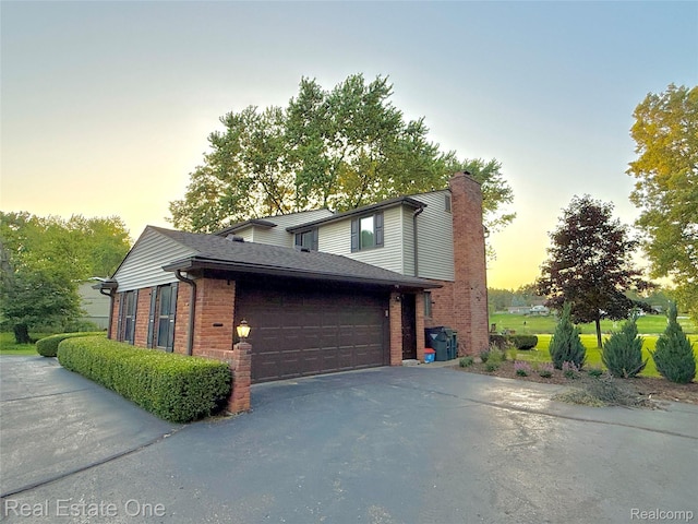 2546 Limerick Ln, Troy, MI 48098 - property exterior at dusk with driveway, brick siding, a chimney, and an attached garage