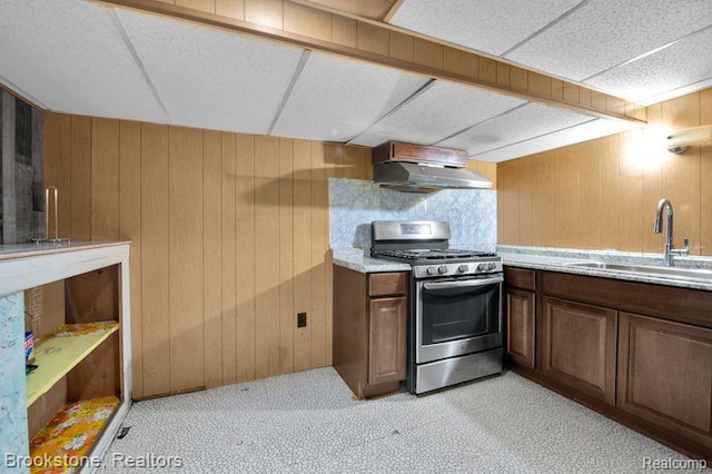 25560 Wexford Ave, Warren, MI 48091 - kitchen featuring stainless steel gas stove, wall chimney exhaust hood, wood walls, a drop ceiling, and light carpet