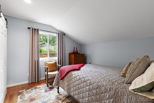 680 Breyman Hwy, Tipton, MI 49287 - bedroom with lofted ceiling, wood finished floors, and a barn door