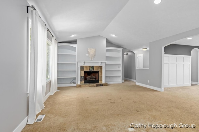 950 Whitetail Ct, Ionia, MI 48846 - unfurnished living room featuring arched walkways, carpet flooring, vaulted ceiling, built in features, and a tile fireplace