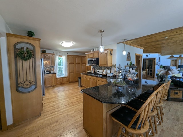 2740 Booth Rd, Au Gres, MI 48703 - kitchen featuring appliances with stainless steel finishes, a peninsula, light wood-style flooring, a kitchen breakfast bar, and decorative backsplash