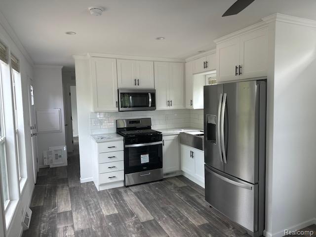 14214 Eastview Dr, Fenton, MI 48430 - kitchen with appliances with stainless steel finishes, light countertops, white cabinetry, decorative backsplash, and dark wood-type flooring