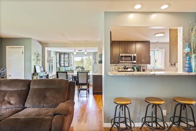 5255 E Holland Rd, Saginaw, MI 48601 - kitchen with stainless steel microwave, open floor plan, a breakfast bar, wood finished floors, and decorative backsplash