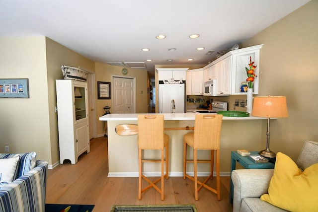 13354 Stover Rd, Charlevoix, MI 49720 - kitchen featuring white appliances, a peninsula, light wood-style floors, recessed lighting, and white cabinets