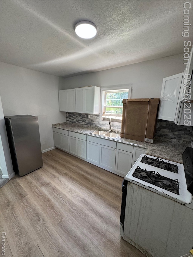 2063 Meade St, Hamtramck, MI 48212 - kitchen with white gas stove, light wood-style flooring, a textured ceiling, decorative backsplash, and white cabinets