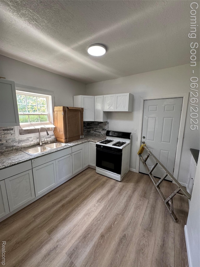 2063 Meade St, Hamtramck, MI 48212 - kitchen featuring white range with gas cooktop, a textured ceiling, decorative backsplash, light wood-style flooring, and white cabinetry