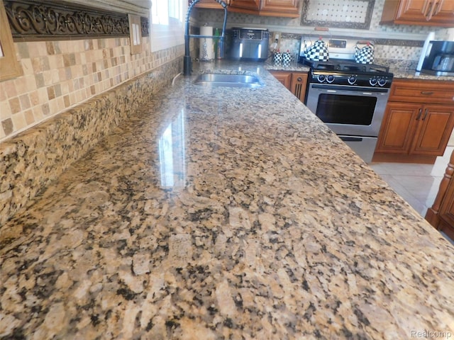 41431 Tarragon Dr, Sterling Heights, MI 48314 - kitchen with stainless steel gas range oven, tasteful backsplash, brown cabinetry, and light stone countertops