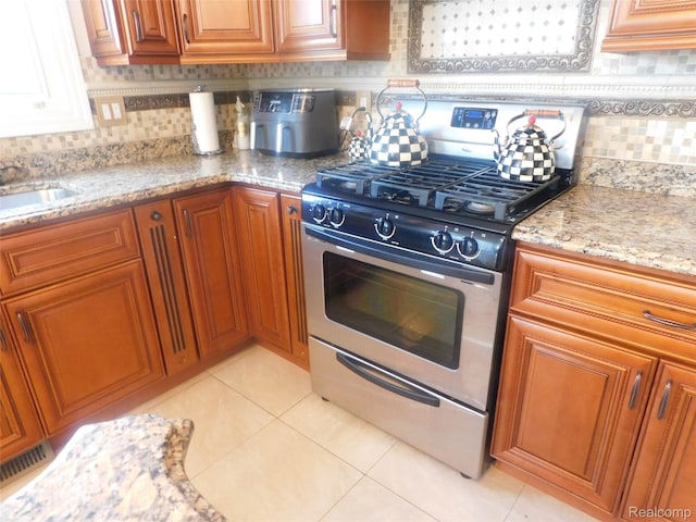 41431 Tarragon Dr, Sterling Heights, MI 48314 - kitchen featuring gas stove, brown cabinets, light tile patterned floors, light stone counters, and decorative backsplash