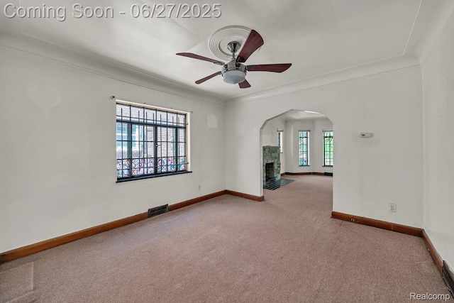 2675 Fleet St, Detroit, MI 48238 - carpeted empty room featuring a ceiling fan, arched walkways, ornamental molding, and a stone fireplace