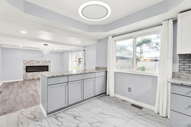 14717 Dane Ct, Sterling Heights, MI 48312 - kitchen featuring light stone countertops, light marble finish flooring, a tile fireplace, a peninsula, and gray cabinets
