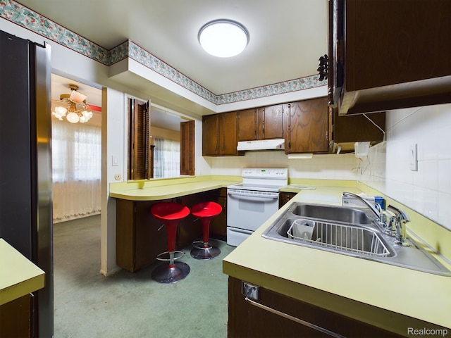 1023 Normandy Terrace Dr, Flint, MI 48532 - kitchen with white electric range oven, under cabinet range hood, dark brown cabinetry, light countertops, and tasteful backsplash