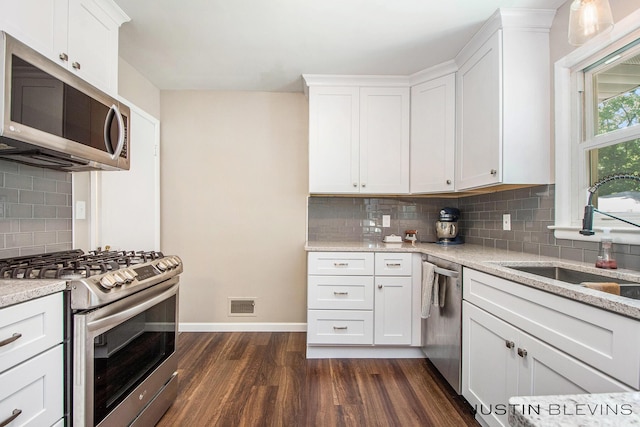 1538 10th St NW, Grand Rapids, MI 49504 - kitchen with appliances with stainless steel finishes, dark wood-style flooring, decorative backsplash, and white cabinetry