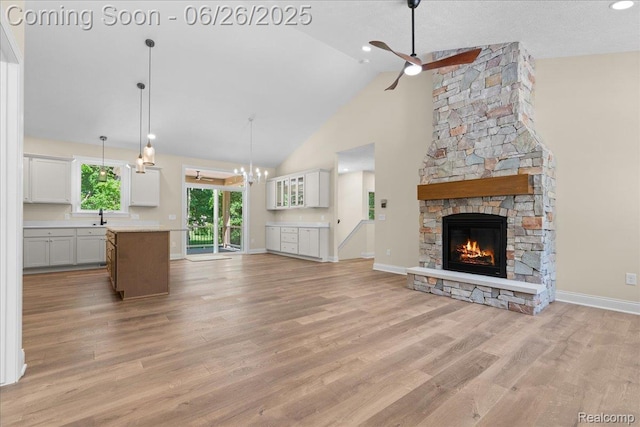 917 Chickasaw Dr, Mason, MI 48854 - unfurnished living room featuring a stone fireplace, a ceiling fan, light wood-style floors, high vaulted ceiling, and a chandelier