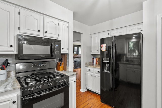 7154 Sandpiper St, Portage, MI 49024 - kitchen with black appliances, white cabinetry, light wood-style flooring, and light stone counters
