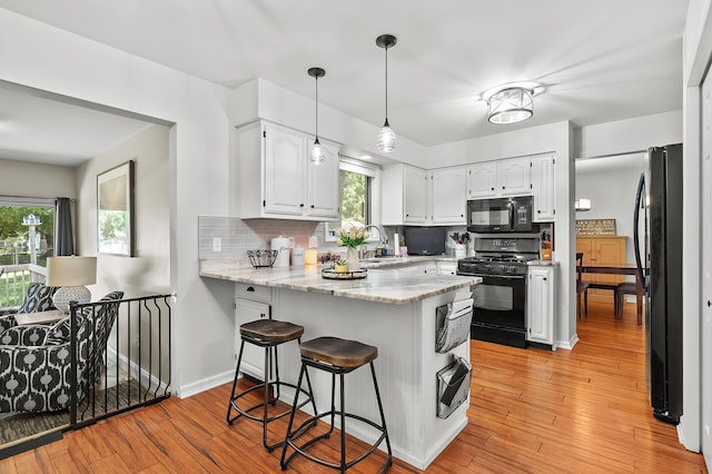 7154 Sandpiper St, Portage, MI 49024 - kitchen with black appliances, a peninsula, white cabinets, light wood-style flooring, and decorative backsplash