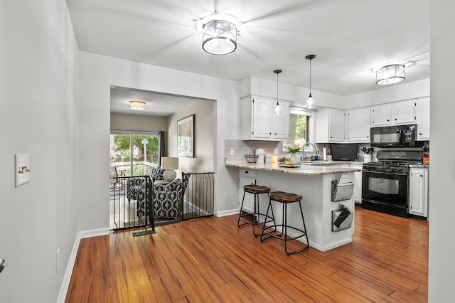 7154 Sandpiper St, Portage, MI 49024 - kitchen with black appliances, white cabinets, a peninsula, backsplash, and a breakfast bar
