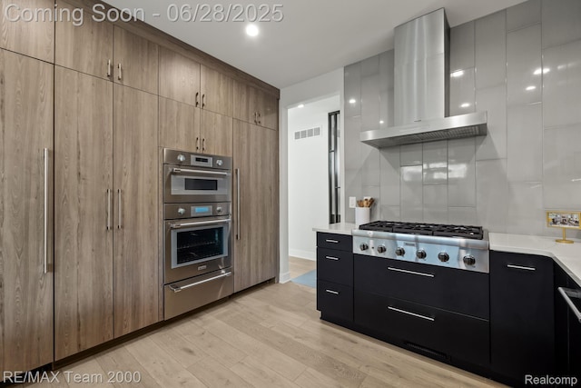 927 Ann St, Birmingham, MI 48009 - kitchen featuring wall chimney exhaust hood, appliances with stainless steel finishes, a warming drawer, light countertops, and light wood-style flooring