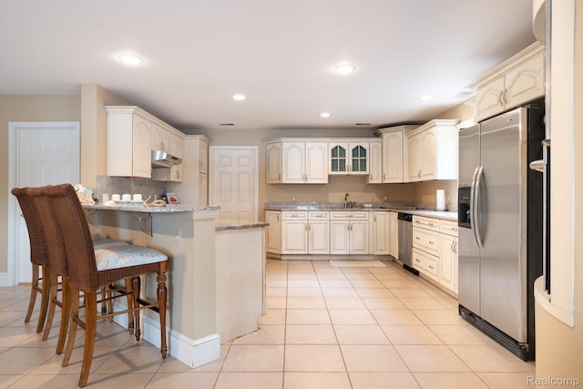 3831 Woodland Dr, Highland, MI 48356 - kitchen featuring stainless steel appliances, a peninsula, under cabinet range hood, a kitchen breakfast bar, and light tile patterned floors