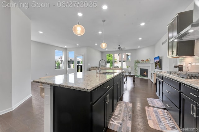 38731 Chasewood Ct, Farmington Hills, MI 48335 - kitchen with wall chimney range hood, stainless steel gas stovetop, open floor plan, a warm lit fireplace, and ceiling fan