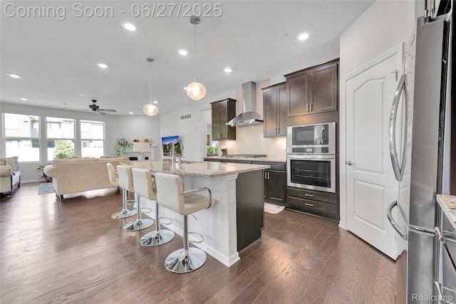 38731 Chasewood Ct, Farmington Hills, MI 48335 - kitchen featuring stainless steel appliances, wall chimney exhaust hood, open floor plan, a kitchen bar, and light stone countertops